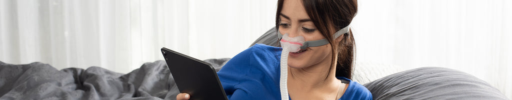 Woman wearing AirFit N30 mask and looking at iPad in bed